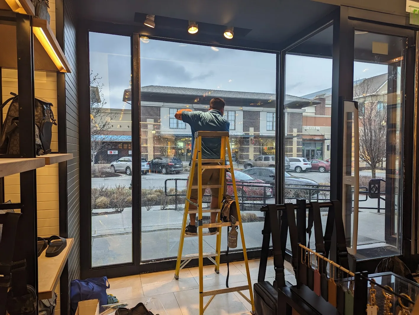 Installer on a ladder applying security film to tall storefront glass