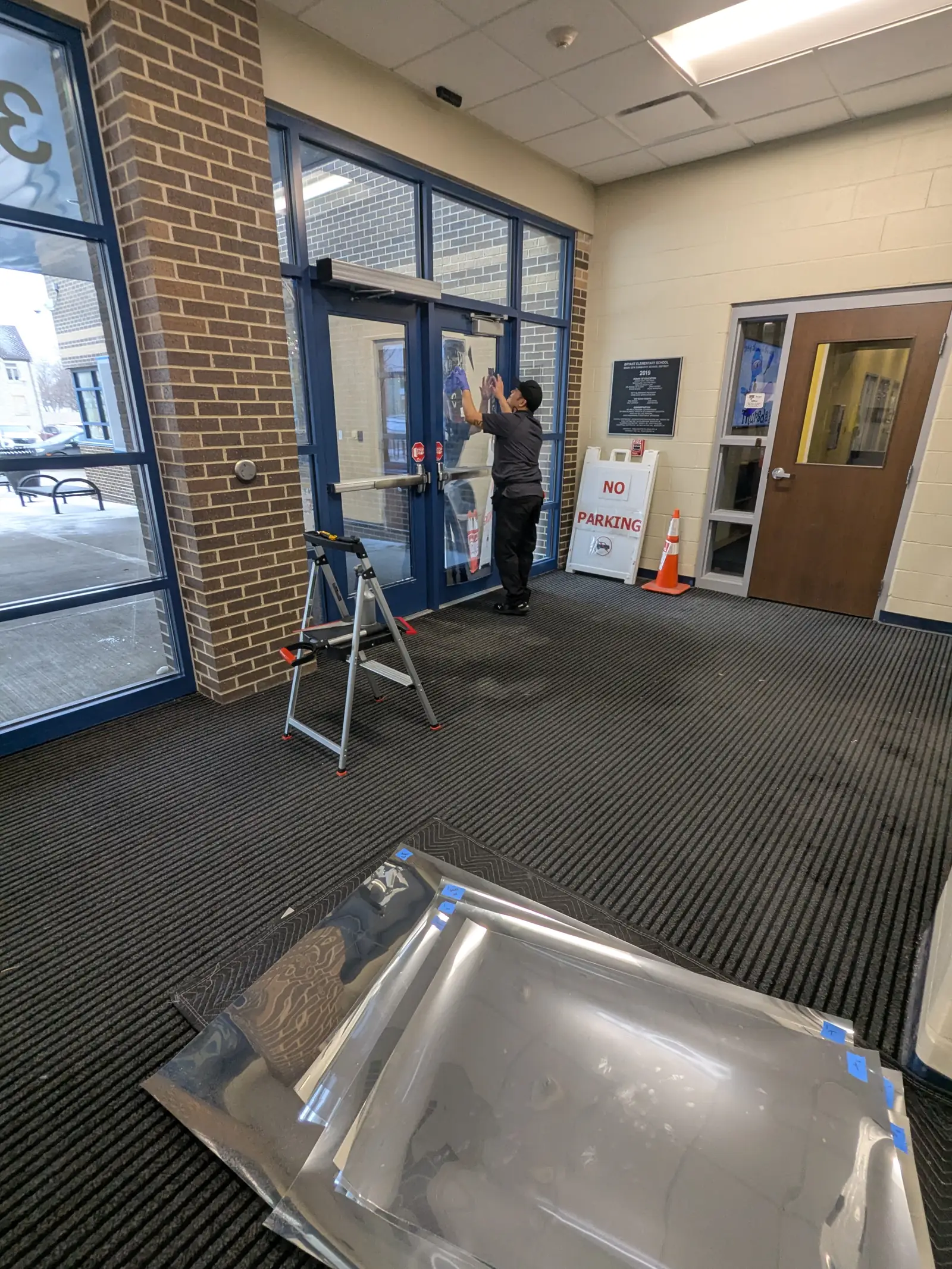 Installer applying security film to school entrance glass with film rolls staged on the floor