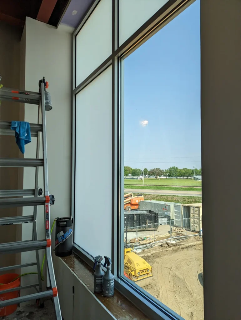 Tall glazing with frosted lower panes and clear upper glass during a window film installation, with ladder and tools nearby