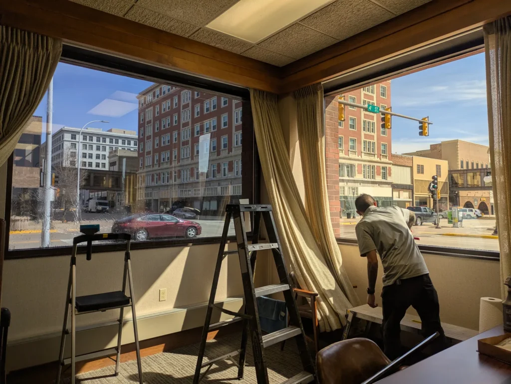 Installer applying window film to large corner office windows overlooking a downtown street