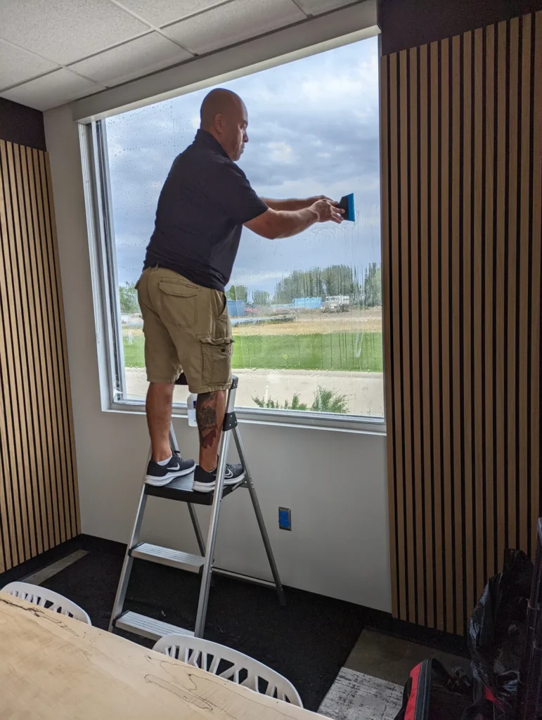 Installer on a step ladder squeegeeing window film onto a large office window
