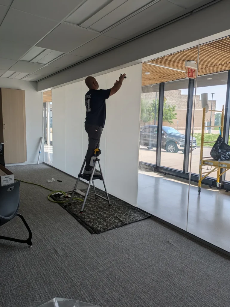Installer on a step ladder applying frosted film to a long interior glass wall
