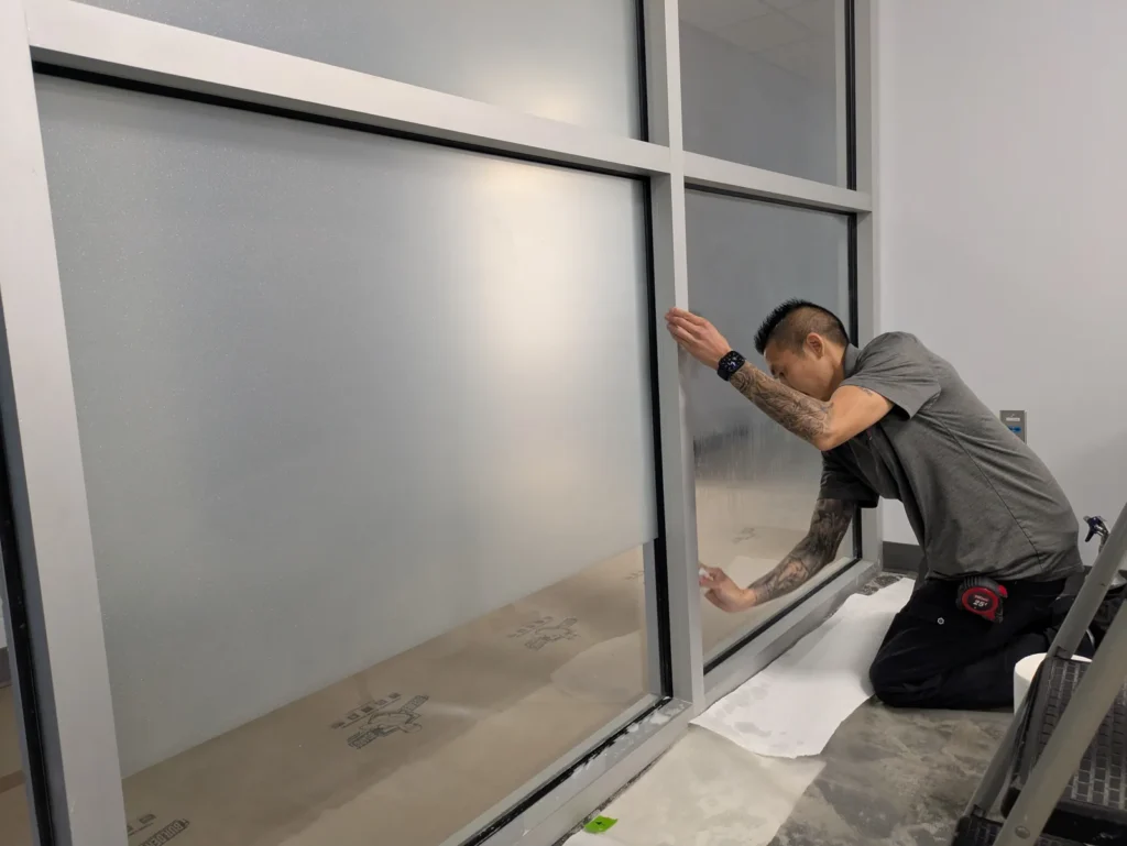 Installer kneeling to apply frosted privacy film to an interior glass partition