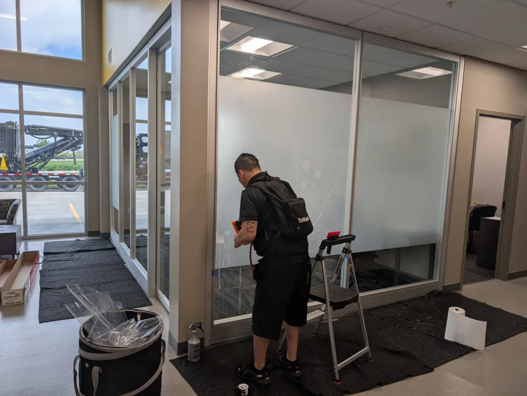 Installer applying frosted privacy film to an office glass wall, leaving clear glass along the top
