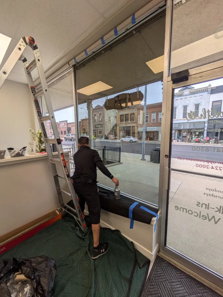 Installer on a ladder applying window film to tall storefront glass beside the entry door