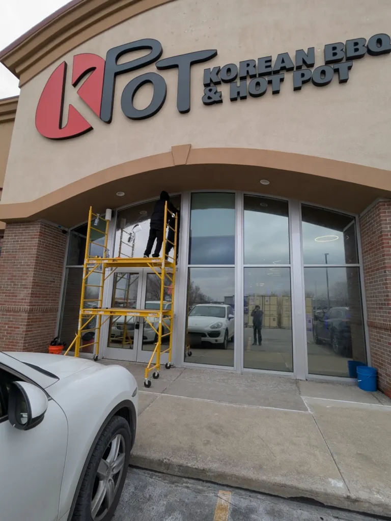 Installer on scaffolding applying window film to the K-Pot Korean BBQ & Hot Pot storefront in Sioux Falls