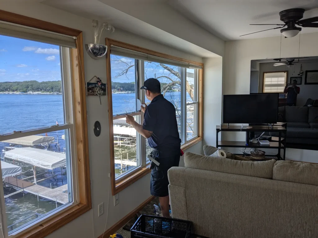 Installer applying window film to double-hung windows overlooking a lake and boat docks