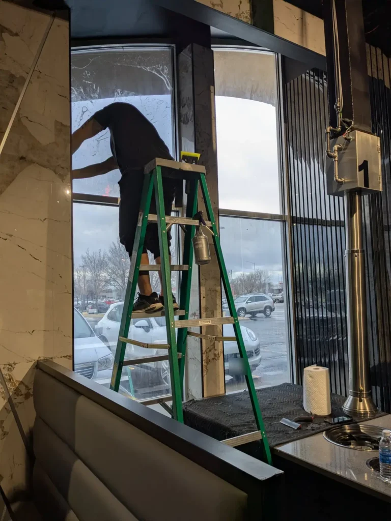 Installer applying solar window film to tall west-facing windows at K-Pot Korean BBQ in Sioux Falls