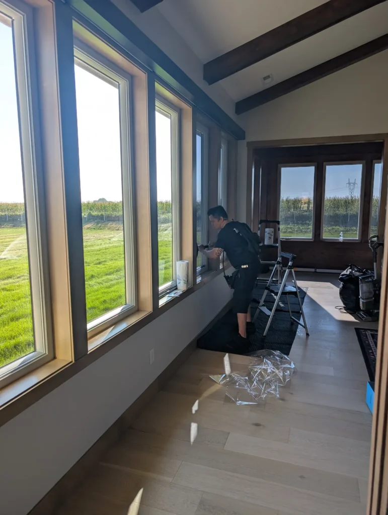 Installer applying solar window film along a long run of sunroom windows facing open farmland