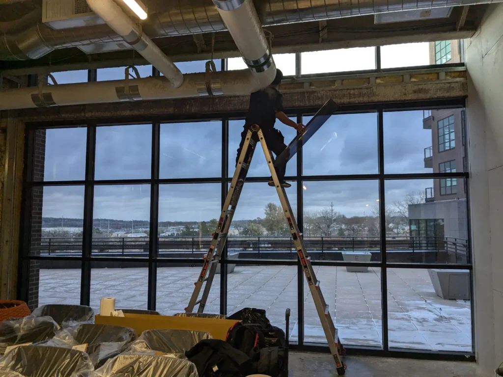 Installer on a ladder applying one-way mirror film to a large window wall at the Steel District in Sioux Falls